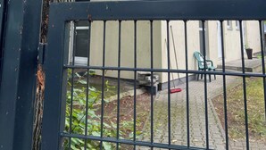 Un bâtiment doté d’une entrée fermée par un portail, d’un chemin pavé et d’un arbre.