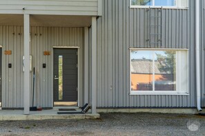 A building with a grey exterior, a black door, and a window with blinds. - Cozy and peaceful apartment in Äkäslompolo (Äkäslompolo)