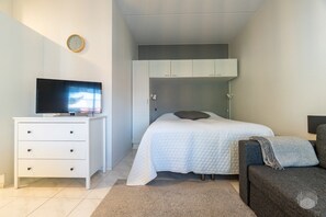 A bedroom with a bed, a TV on a dresser, a clock on the wall, and a chair. - Cozy and peaceful apartment in Äkäslompolo (Äkäslompolo)
