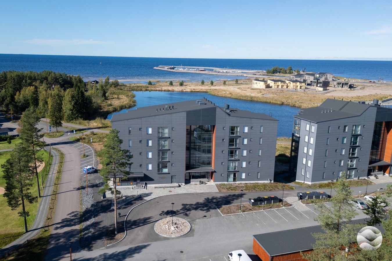 A modern building complex with multiple floors, parking areas, and a view of the sea.