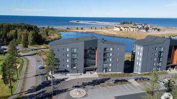 A modern building complex with multiple floors, parking areas, and a view of the sea.
