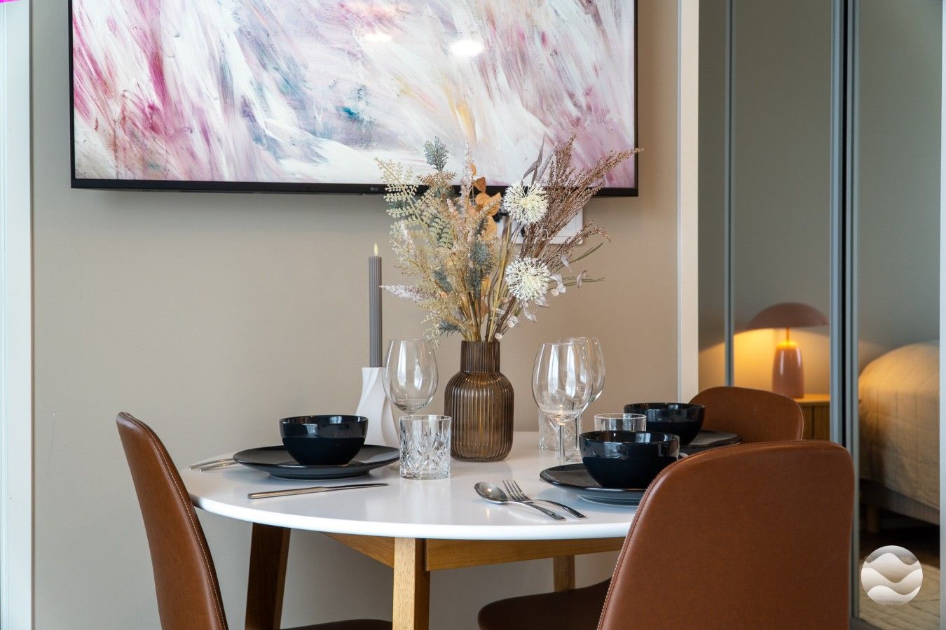 A dining table set with black bowls, wine glasses, and a vase with dried flowers.