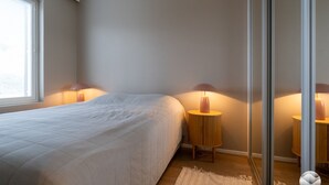 Quarto com cama, duas mesas de cabeceira com luminárias, janela e porta.