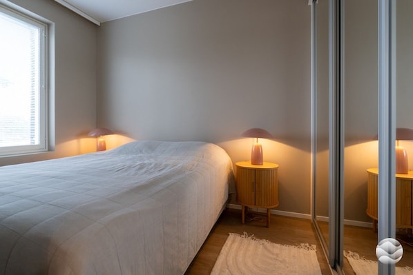 A bedroom with a bed, two bedside tables with lamps, a window, and a door.