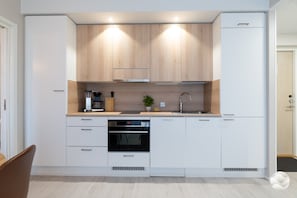 A modern kitchen with white cabinetry, a built-in oven, a coffee machine, and a sink.