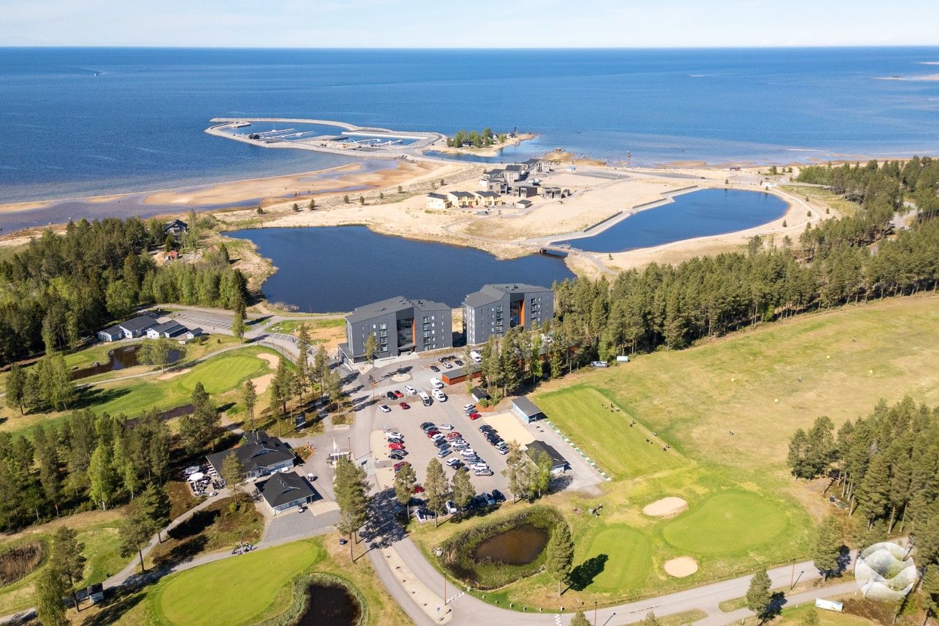 Vista aérea de un complejo turístico con un amplio estacionamiento, varias edificaciones y una masa de agua.