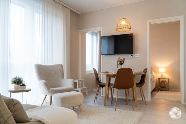 A modern living room with a sofa, armchair, ottoman, dining table with chairs, a TV mounted on the wall, and a lamp on a side table. - Marinan Portin Majakka B46 by Holiday in Kalajoki (Kalajoki)
