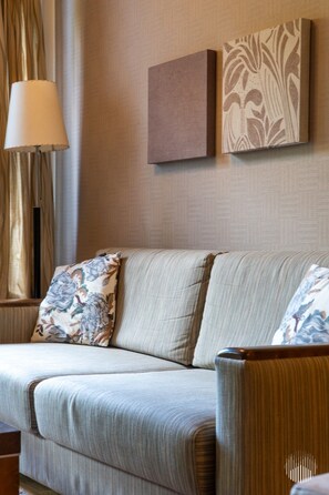 A sofa with floral cushions, a lamp, and two wall-mounted artworks in a room with patterned wallpaper.