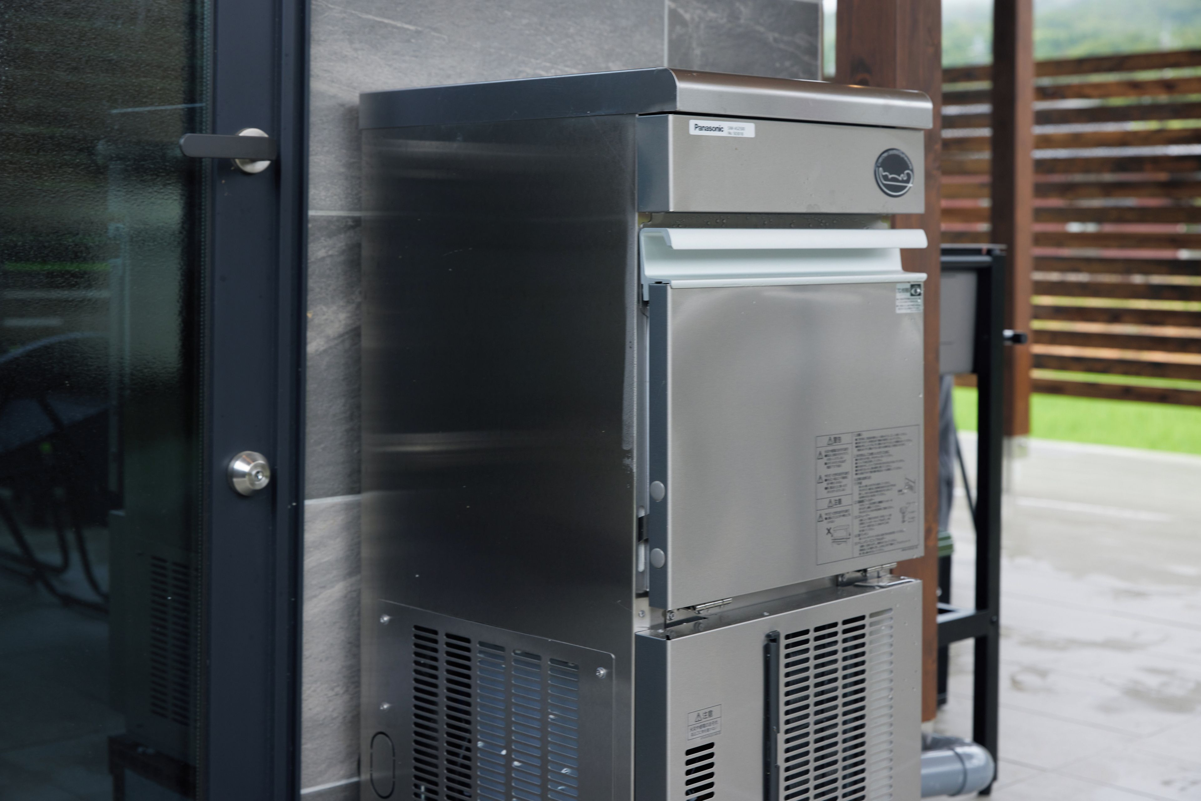 A commercial kitchen with stainless steel appliances, including a refrigerator and a microwave, with a metal door and ventilation grilles.