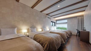 A hotel room with four beds aligned in a row, a large window with curtains, and a wooden floor.