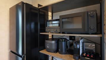 A compact kitchen with a black refrigerator, a microwave, a coffee maker, and a rice cooker.