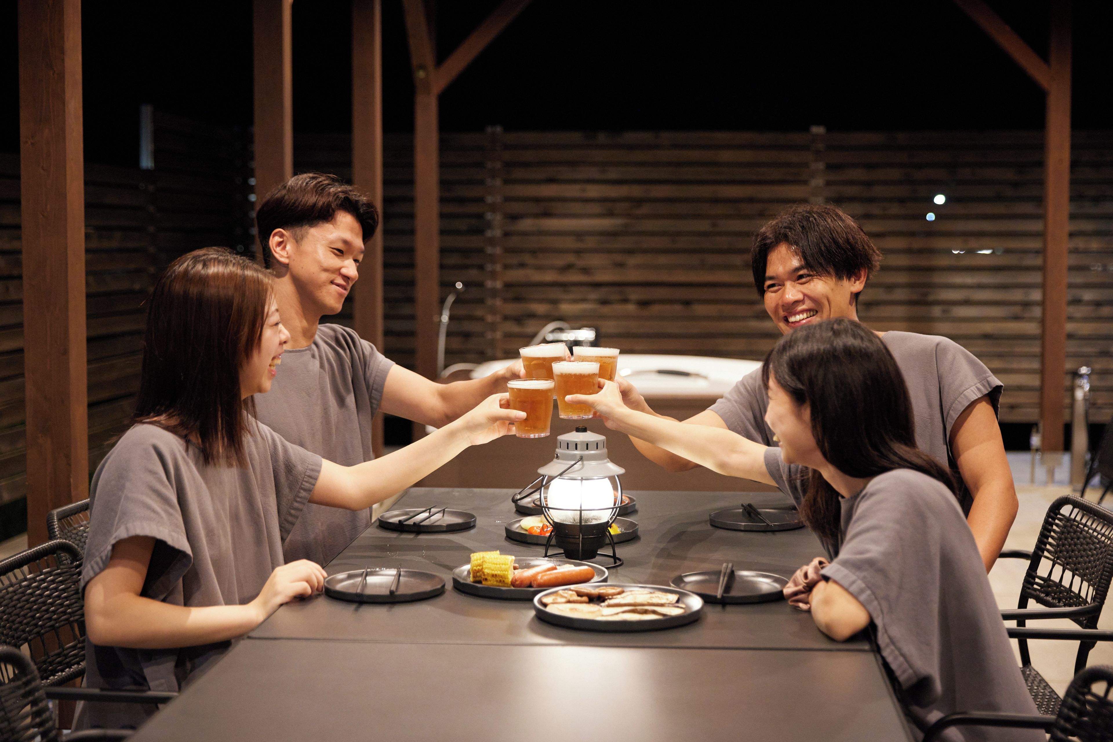 A group of people toasting with glasses at a table with food and a portable heater.