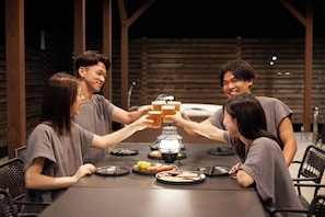 Un grupo de personas brindando con copas en una mesa con comida y un calentador portátil.