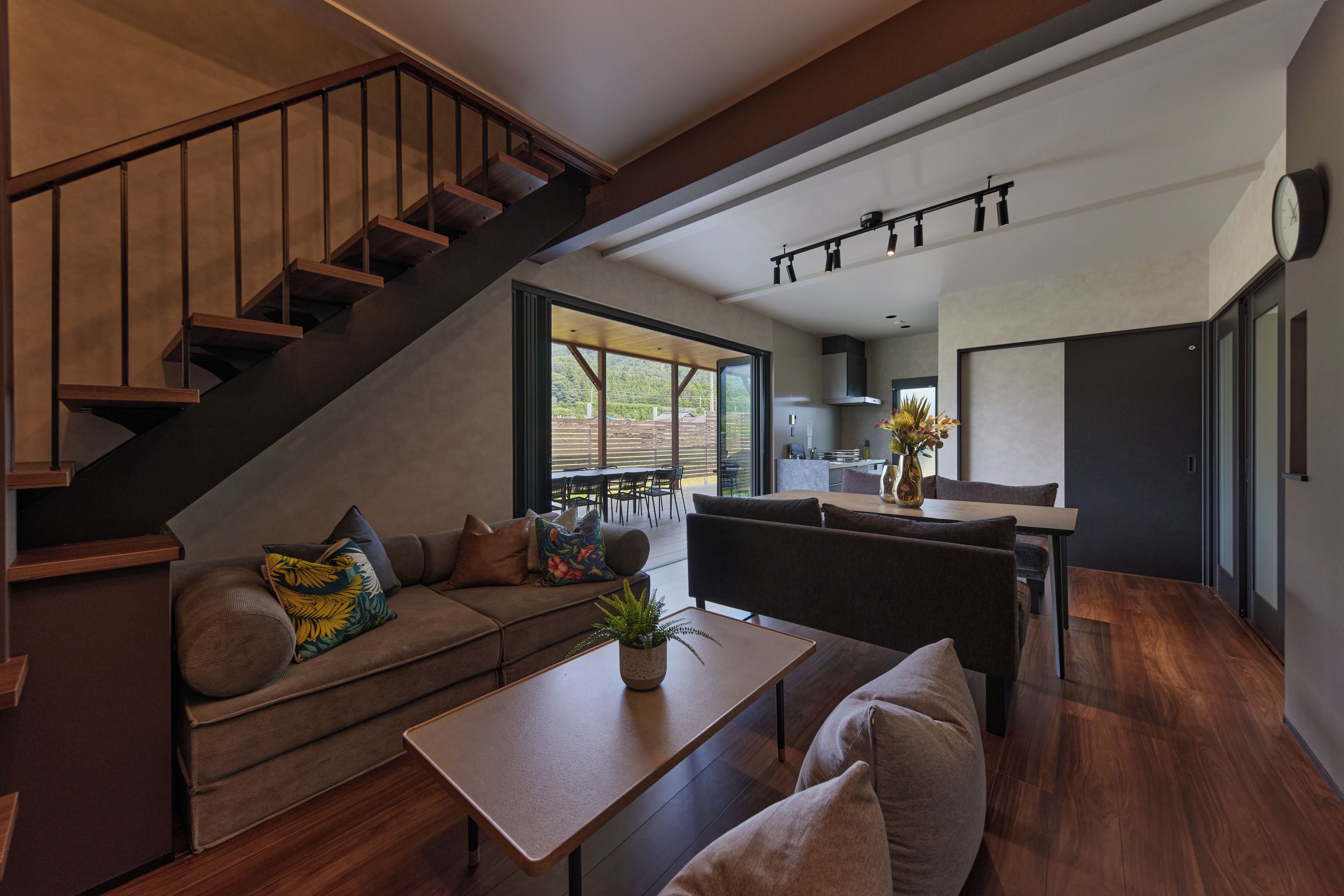 Un espacio moderno para vivir con escalera, sofá, mesa de comedor y zona de cocina.