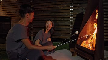 Two people roasting marshmallows over a wood fire in a backyard.