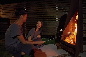 Two people roasting marshmallows over a wood fire in a backyard.