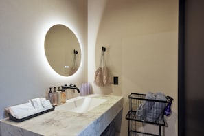 A bathroom with a marble sink, a round mirror, and a towel rack.