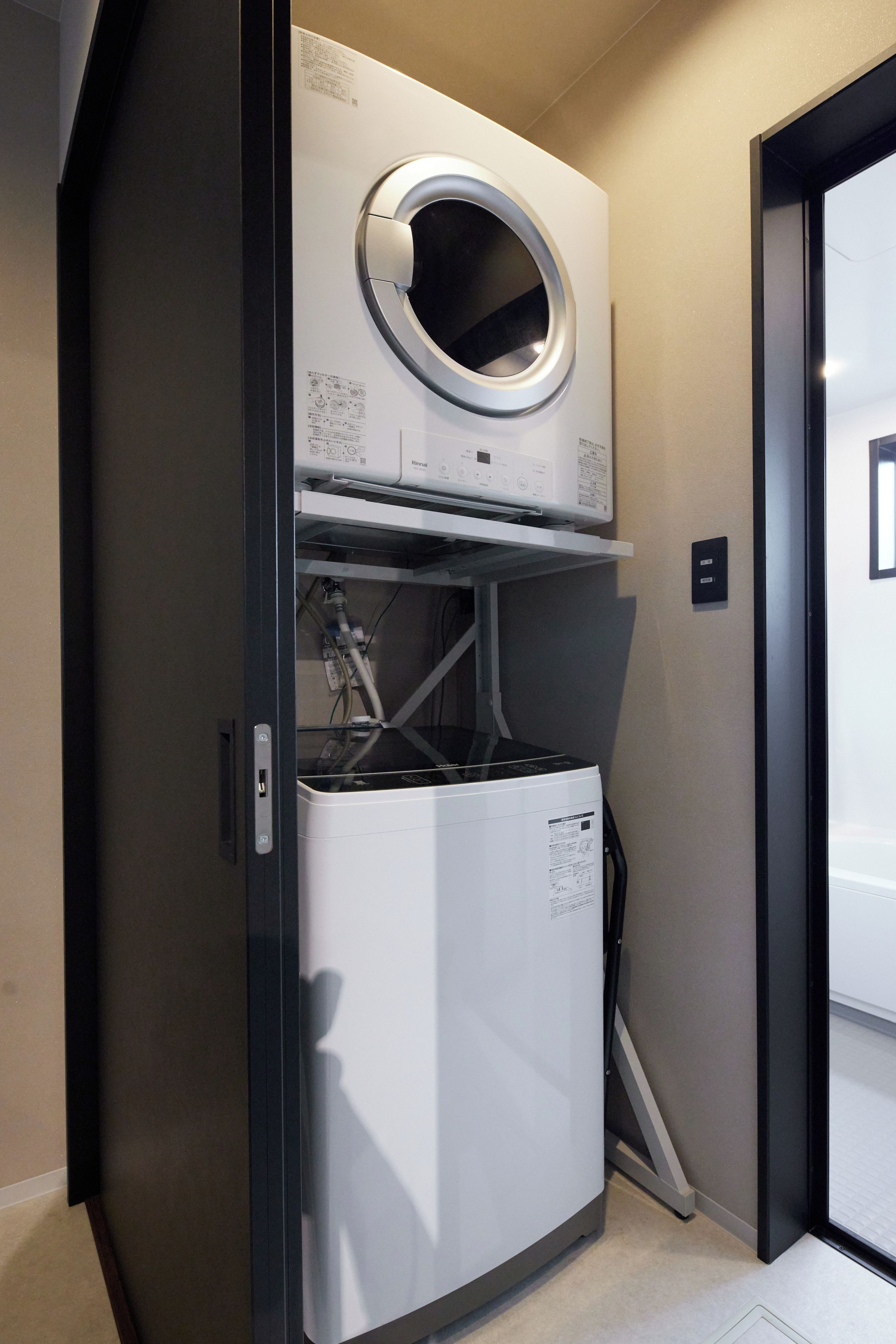 A compact laundry room with a front-loading washer and dryer, a built-in dryer vent, and a door leading to another room.
