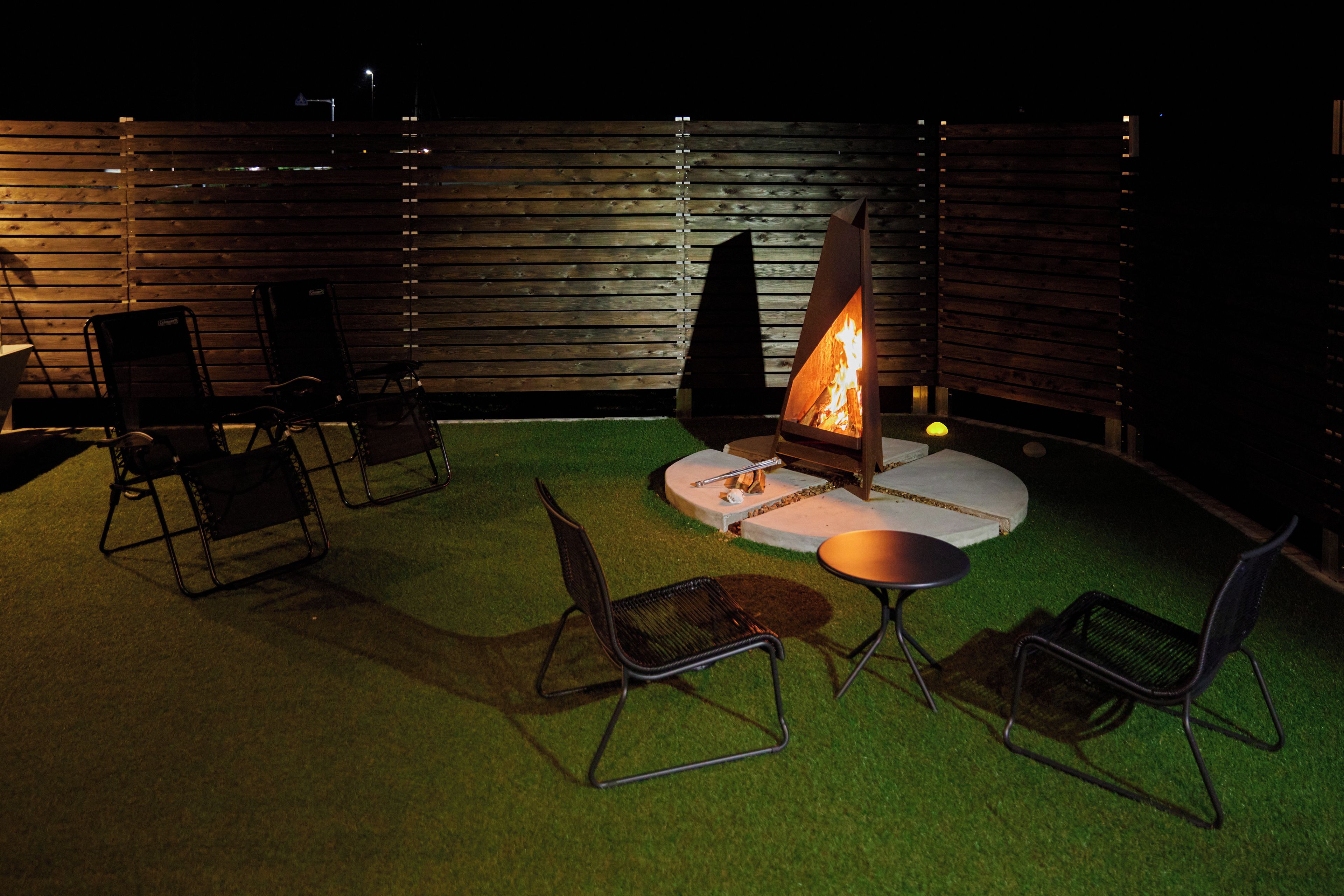 An outdoor seating area with a fire pit, chairs, and a table on artificial grass.