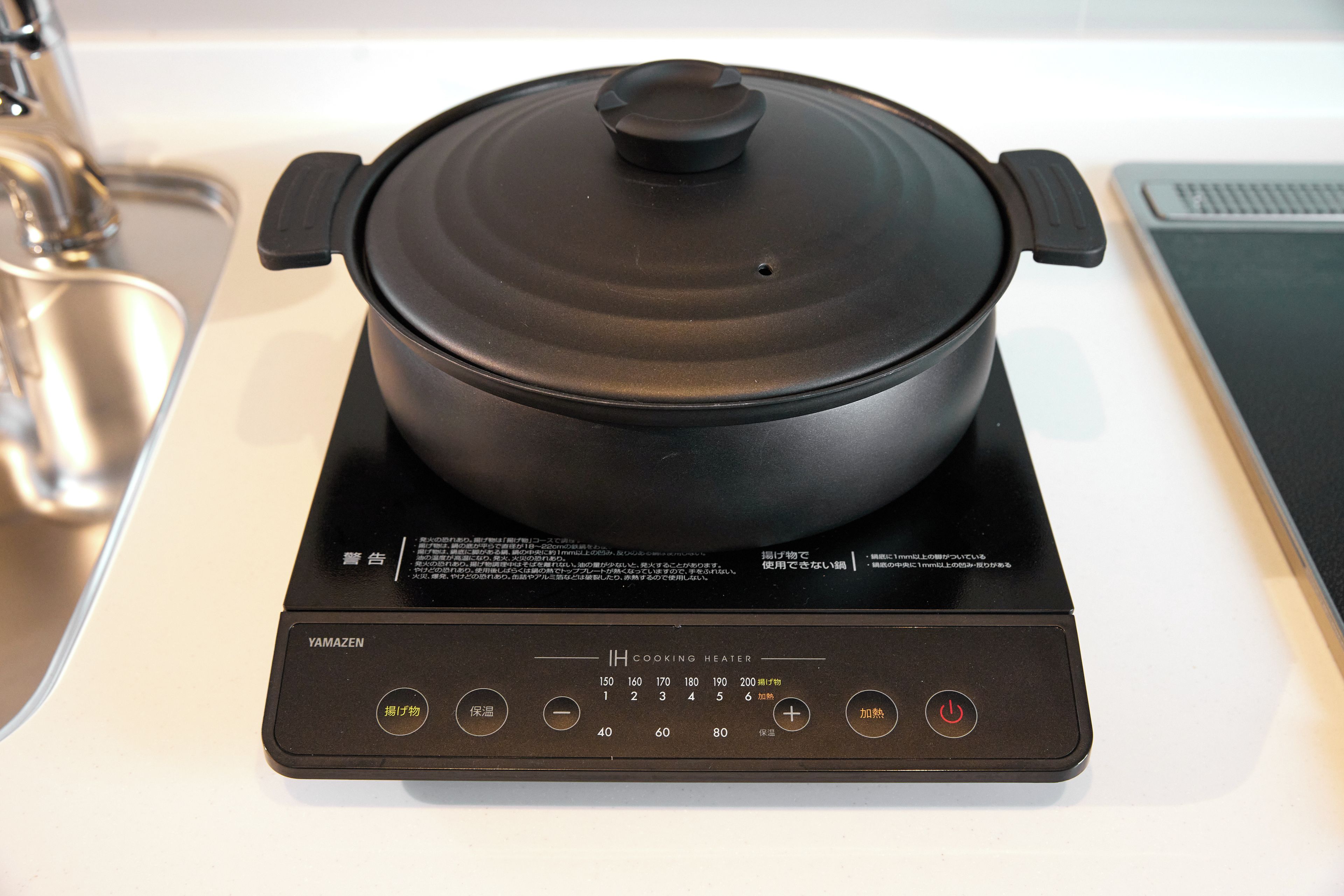 Un calentador IH negro con una olla encima, botones de control y una pantalla digital.
