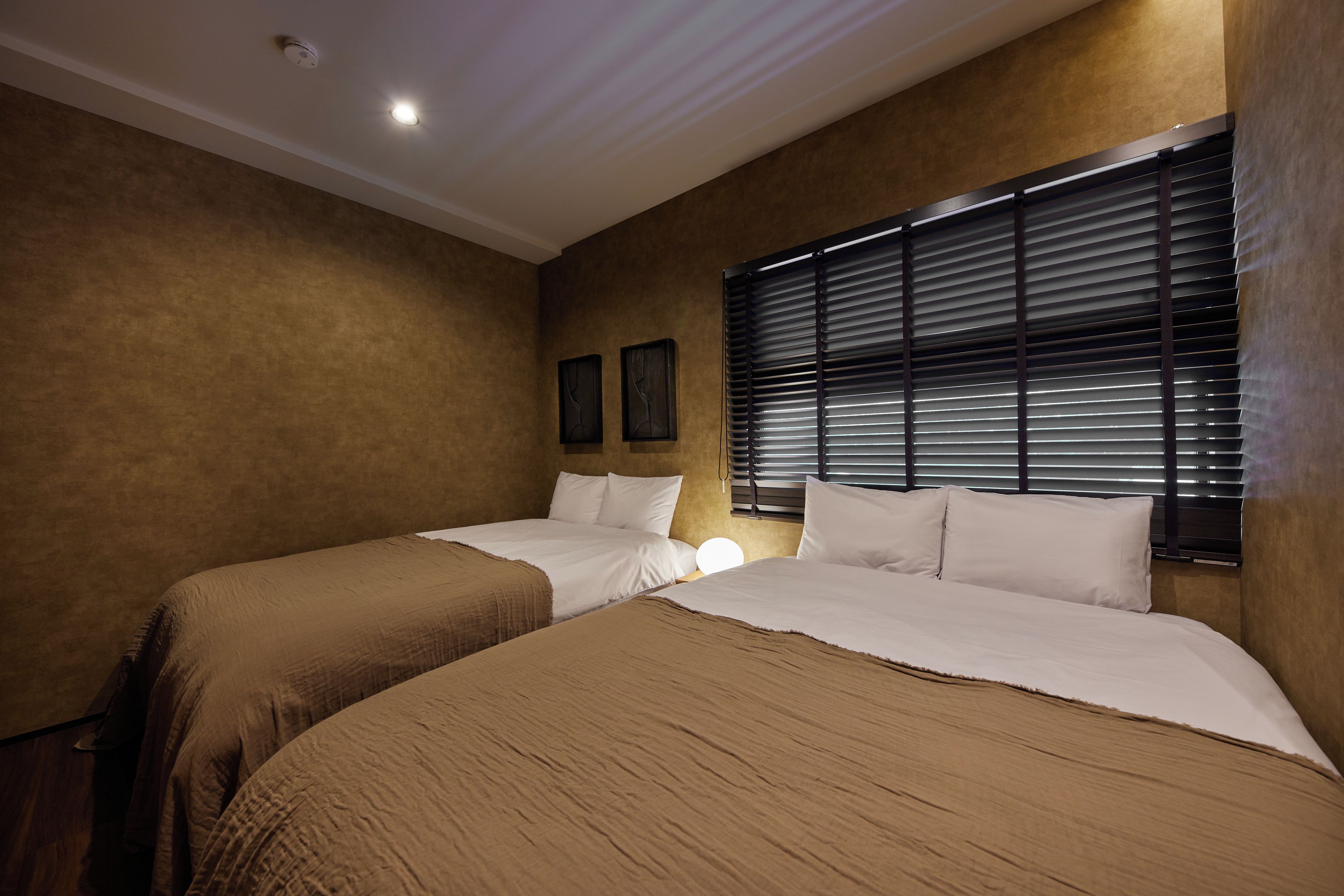 Habitación de hotel con dos camas, una lámpara en el techo y una ventana con persianas.