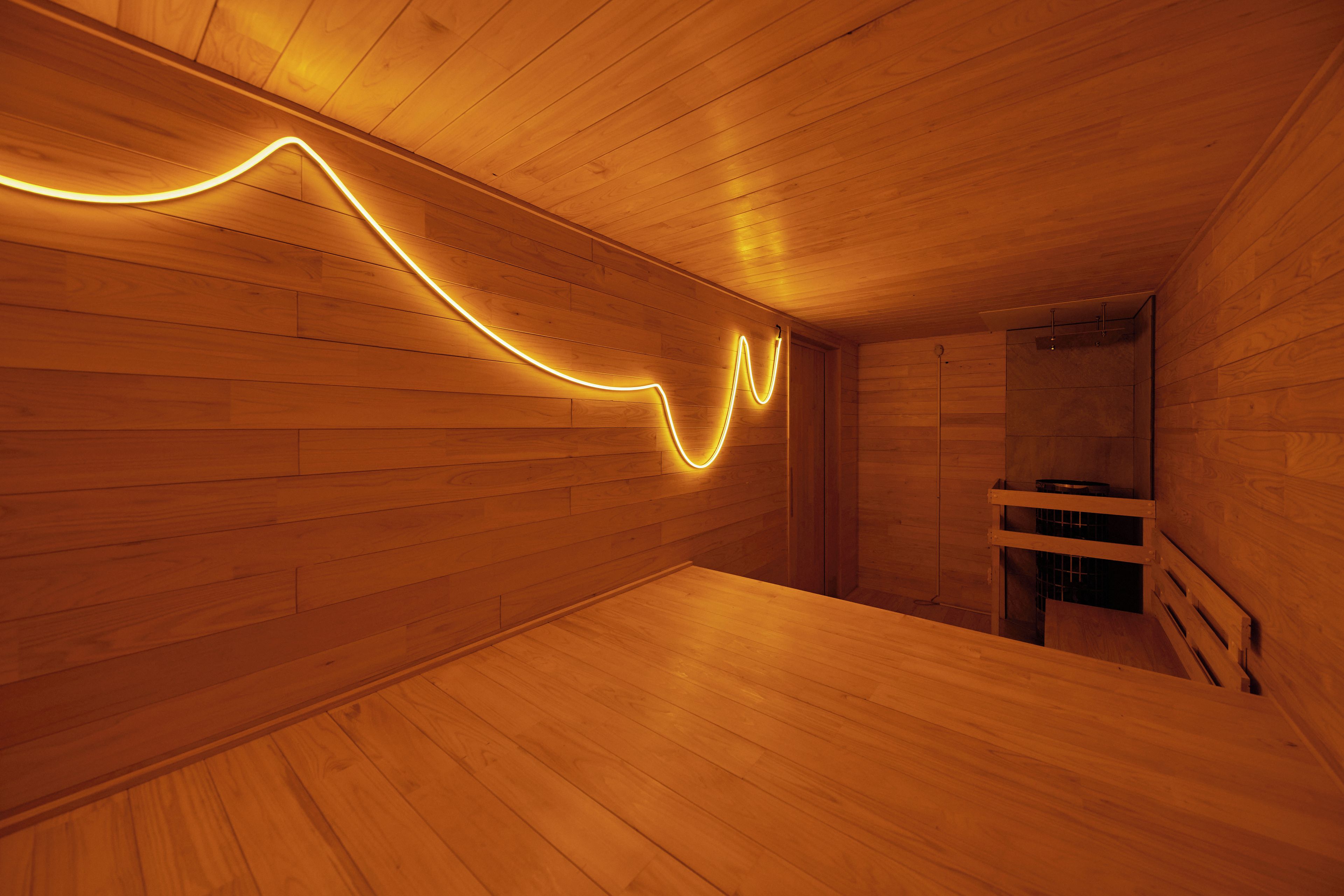 A wooden interior with a curved light installation on the wall and a wooden bench.