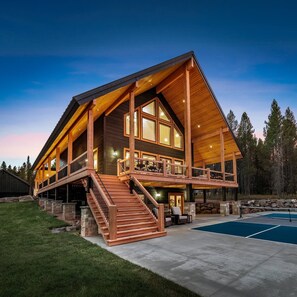 Una cabaña grande de madera, de varios niveles, con una escalera destacada, una piscina y un área de terraza.