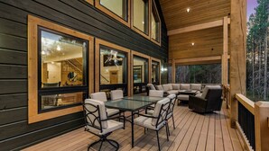 A wooden deck with a glass table and chairs, a sofa, and large windows. - Emerald Pines Lodge+HotTub+Cent AC+20mYellowstone (Island Park)