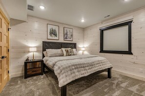 Un dormitorio con una cama, dos mesitas de noche con lámparas, una ventana con persianas y dos cuadros enmarcados en la pared.
