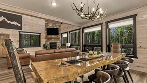 A modern living room with a large wooden dining table, leather sofa, and a fireplace. - Emerald Pines Lodge+HotTub+Cent AC+20mYellowstone (Island Park)