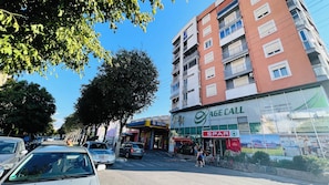 A street view with a multi-story building, a Spar convenience store, and parked cars. - Family apartment in Shkoder: balcony, work corner, free parking (Shkodër)