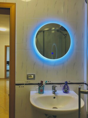 A bathroom with a round mirror, a sink, and a toothbrush holder. - Family apartment in Shkoder: balcony, work corner, free parking (Shkodër)