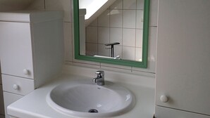 Ein Badezimmer mit weißem Waschbecken, spiegel mit grünem Rahmen und weißen Schränken.