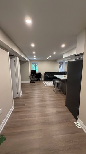 A spacious room with a wooden floor, a black couch, a dining table, and a refrigerator. - Clean comfortable charming Beamsville stay (Lincoln)
