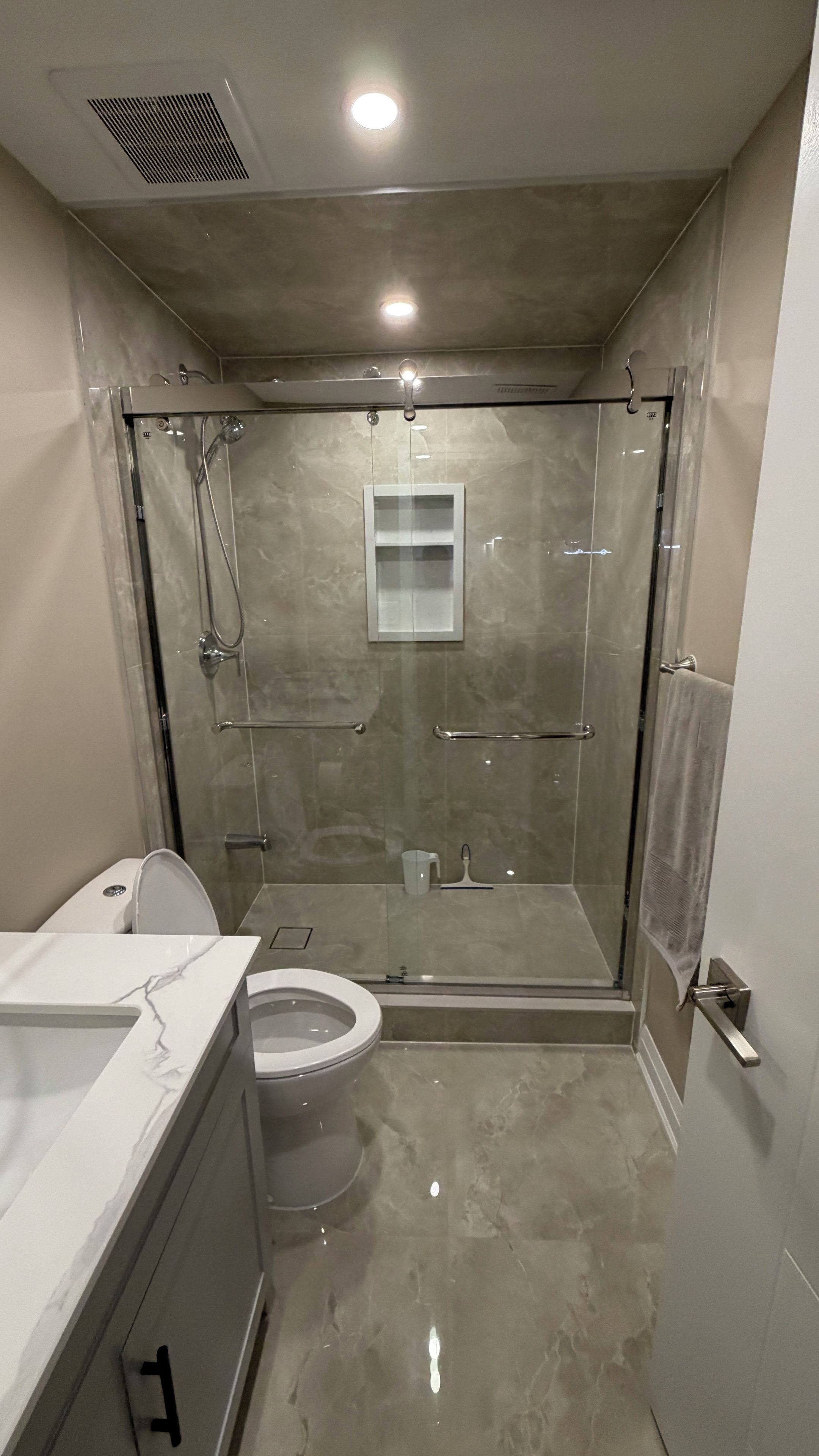 A modern bathroom with a glass-enclosed shower, a toilet, and a vanity with a marble countertop.