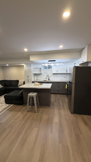 A modern kitchen with a central island, dark-toned cabinets, and a stainless steel refrigerator. - Clean comfortable charming Beamsville stay (Lincoln)