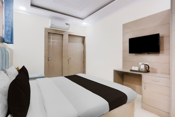 A hotel room with a bed, a TV mounted on the wall, a wardrobe, and an air conditioning unit.