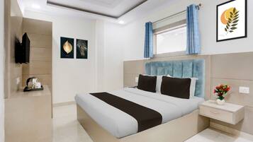 A modern hotel room with a large bed, a bedside table, a nightstand, a window with curtains, and artwork on the walls.