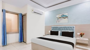 Habitación de hotel con cama, mesita de noche, aire acondicionado de pared, un cuadro y una ventana con cortinas.