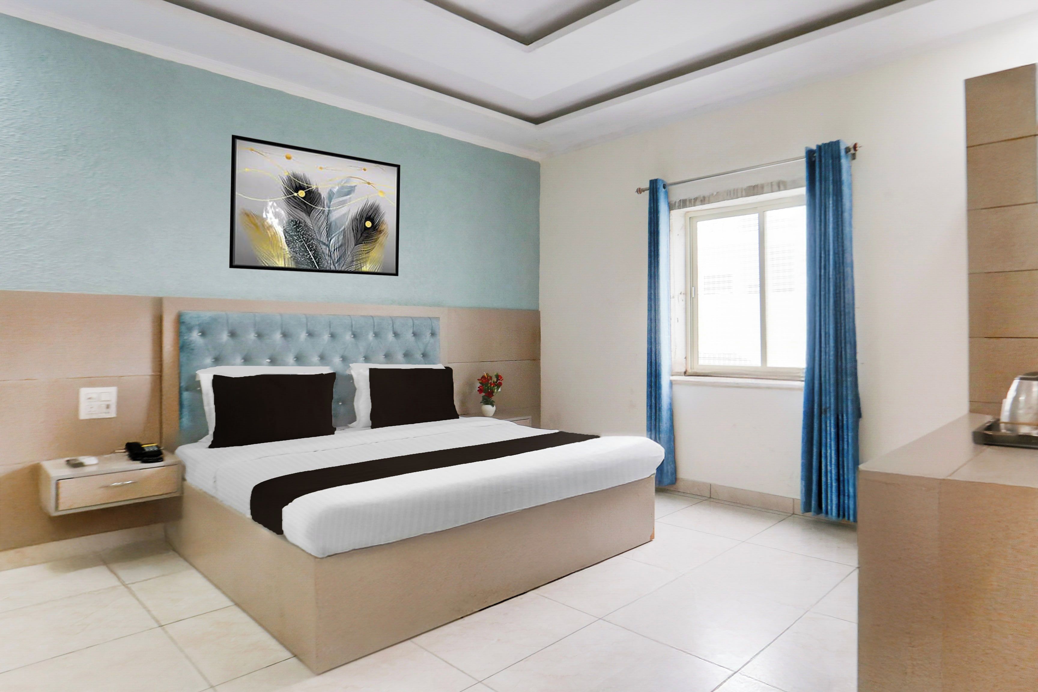 A hotel room with a bed, a nightstand, a wall-mounted artwork, a window with curtains, and a bedside table.