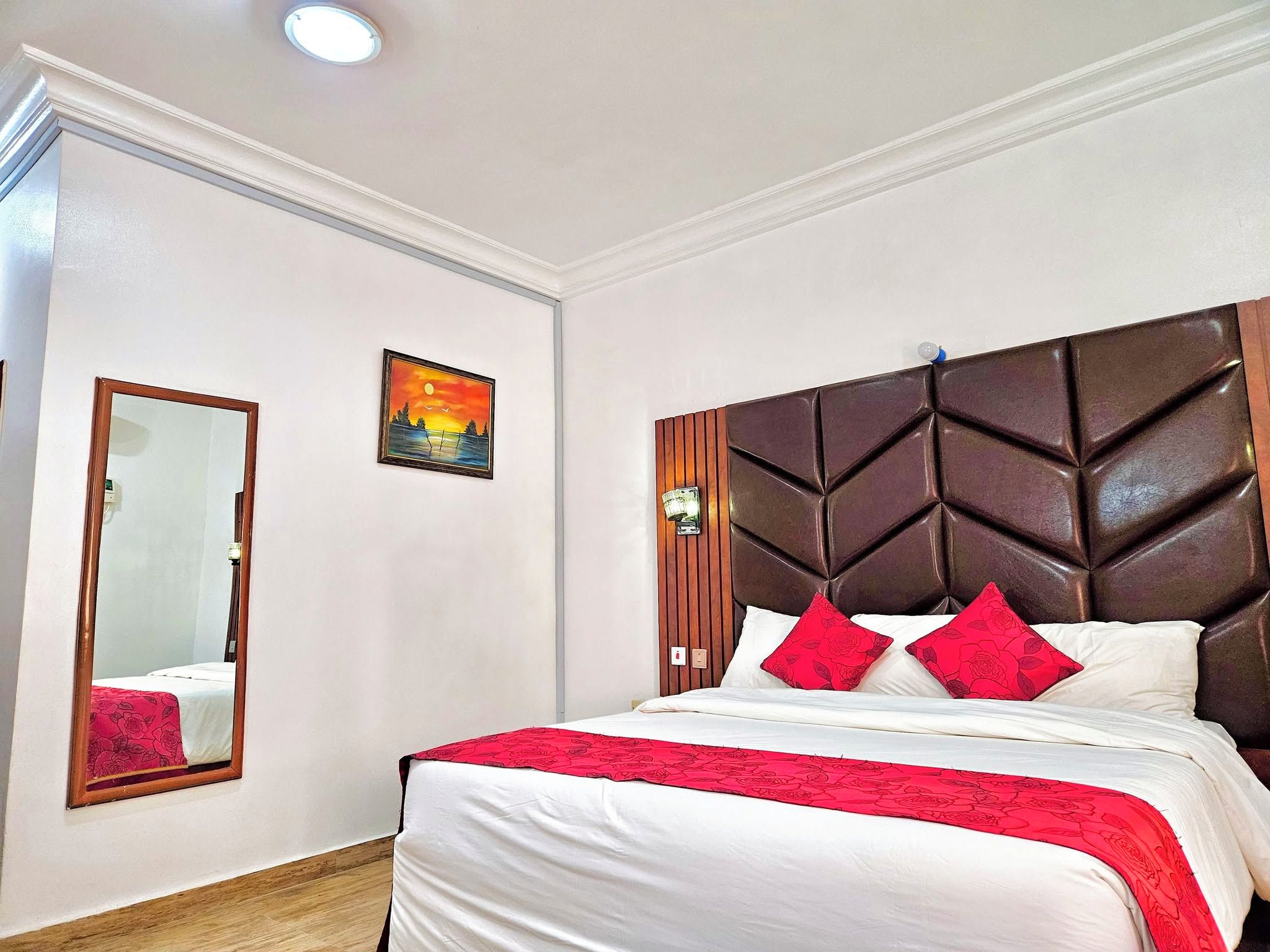 A hotel room with a large bed, a wooden headboard, a mirror, and a painting on the wall.