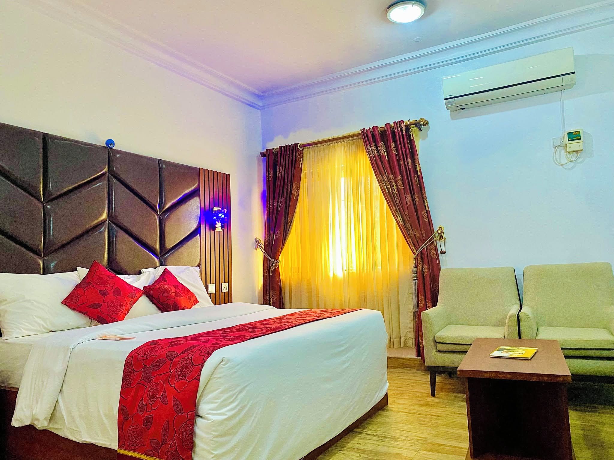 Quarto de hotel com uma cama, uma cadeira, ar condicionado e janela com cortinas.