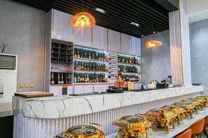 Una zona de bar con mostrador de mármol, varias estanterías con botellas y una fila de taburetes.