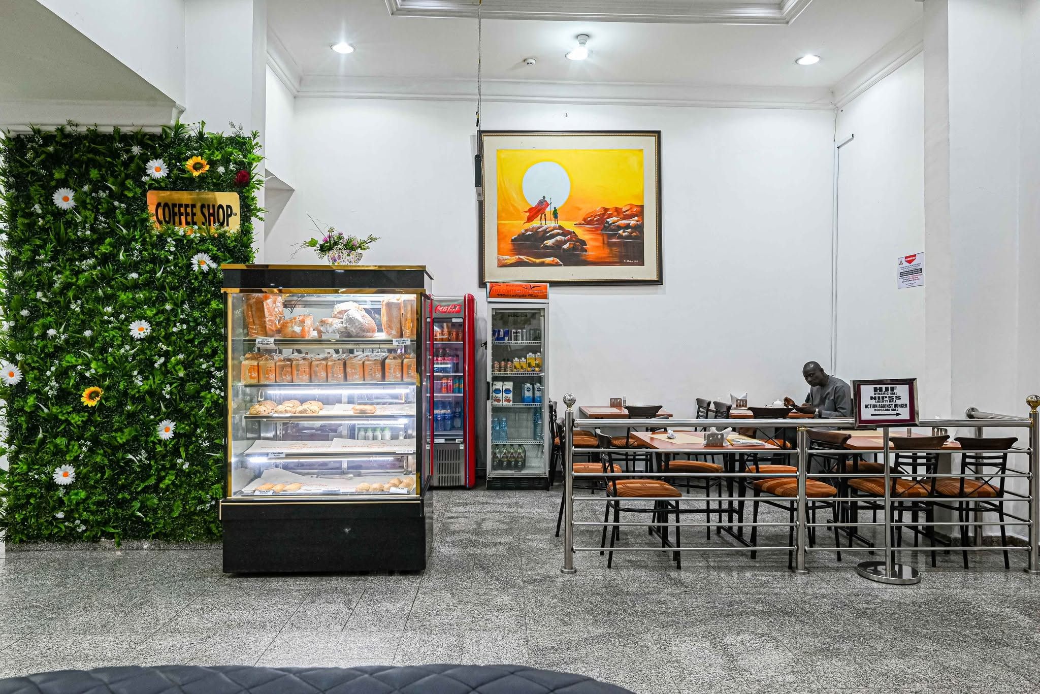 Interior de una cafetería con una vitrina, zona de asientos y un cuadro en la pared.