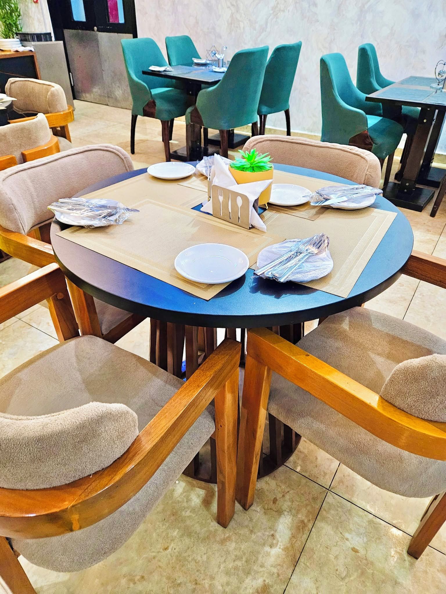 Una mesa redonda con tapa azul, rodeada de sillas con cojines color beige y patas de madera.