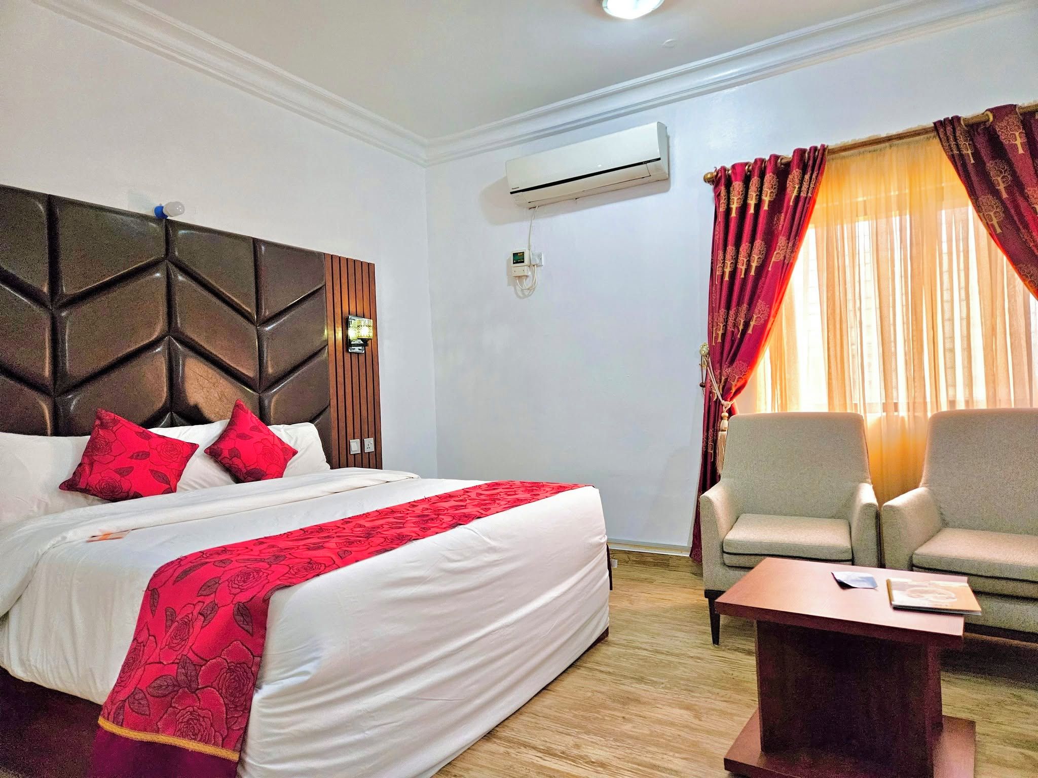 Una habitación de hotel con cama, sofá, mesa de centro, aire acondicionado y ventana con cortinas.