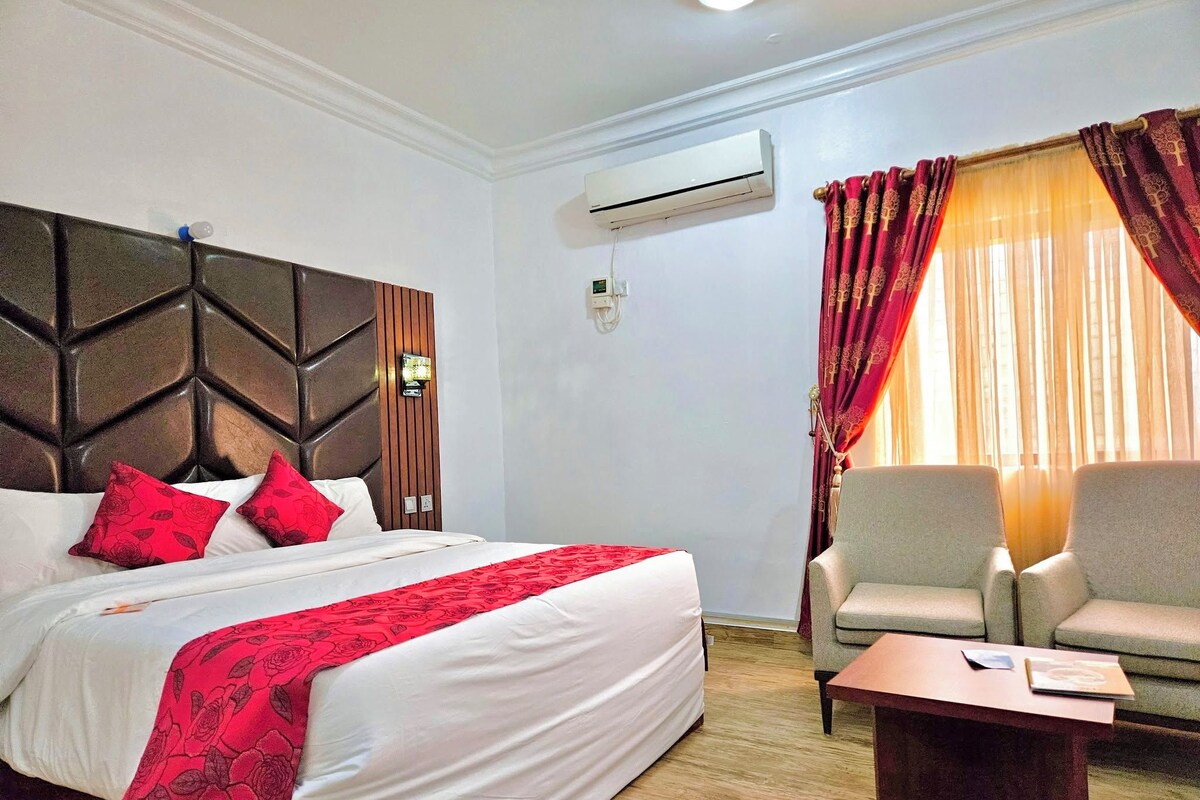 Una habitación de hotel con cama, sofá, mesa de centro, aire acondicionado y ventana con cortinas.