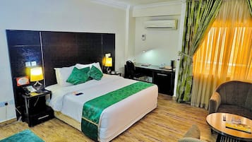 A hotel room with a bed, bedside tables, a desk, a chair, and a small table.
