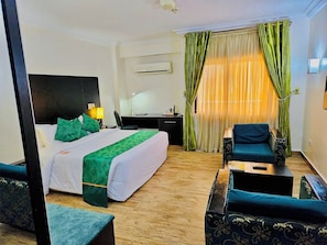A hotel room with a bed, desk, chair, and a view of the outdoors. - Conitnental Exquisite Hotel by Reiz (Abuja)