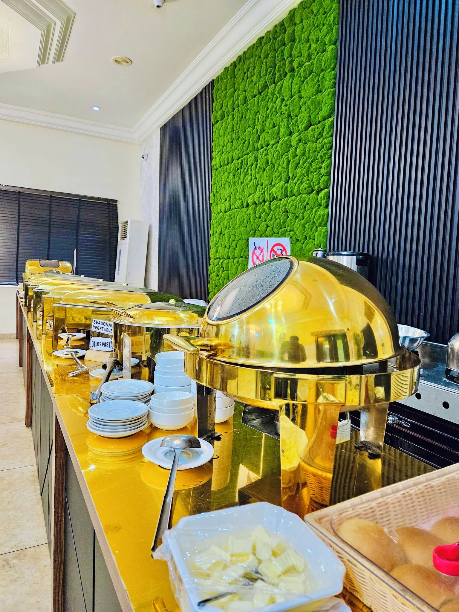 Disposição de buffet com diversos recipientes de comida e uma churrasqueira grande no centro.